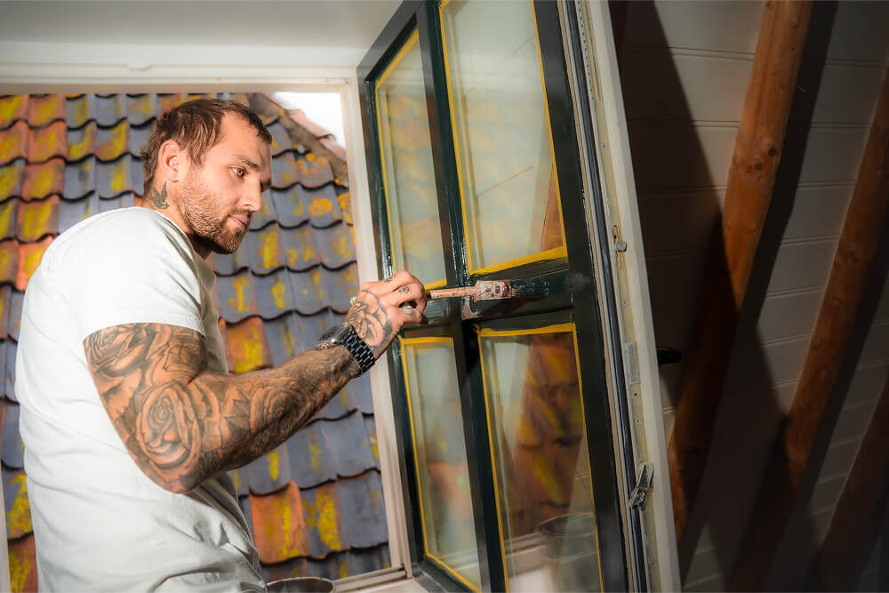 Schilder lakkt de glaslatten van een geopend raam met een platte kwast